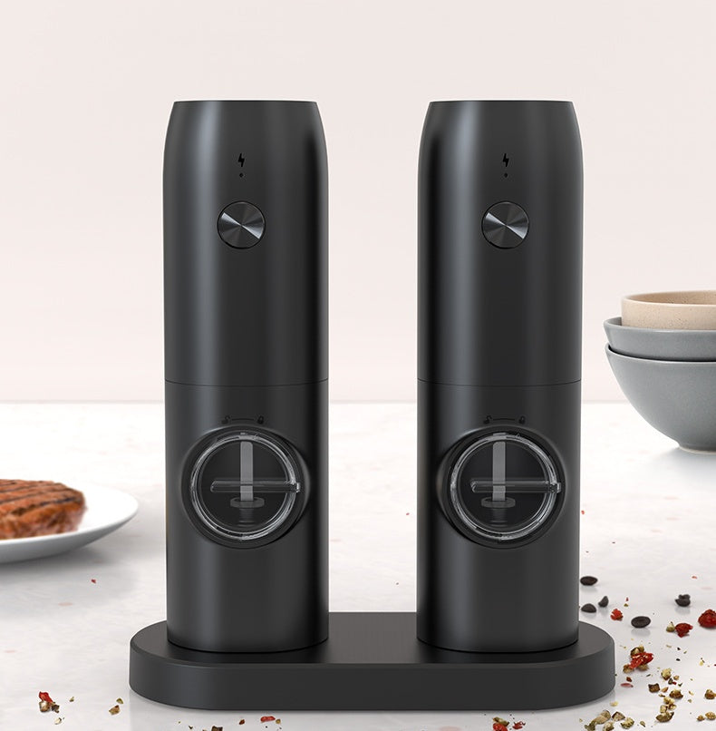 Two black pepper grinders on a white surface with a light background